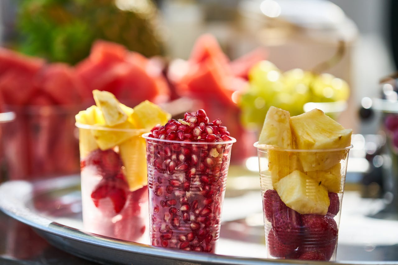 Close-up of colorful fresh fruit cups with pineapple, pomegranate, and strawberries on a bright platter.